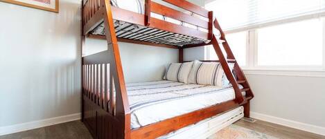 A bunk bed with a wooden frame and white bedding, a patterned rug, and a window with blinds.