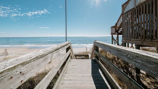 A wooden boardwalk leading to a beach with a clear sky and sun shining. - Ocean Views + Across from Beach Access! (Surf City)