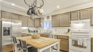 A modern kitchen with stainless steel appliances, wooden cabinets, and a central island with chairs. - Ohana Hut (Colorado Springs)