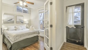 A bedroom with a bed, ceiling fan, artwork, and a view of the outside. - Ohana Hut (Colorado Springs)