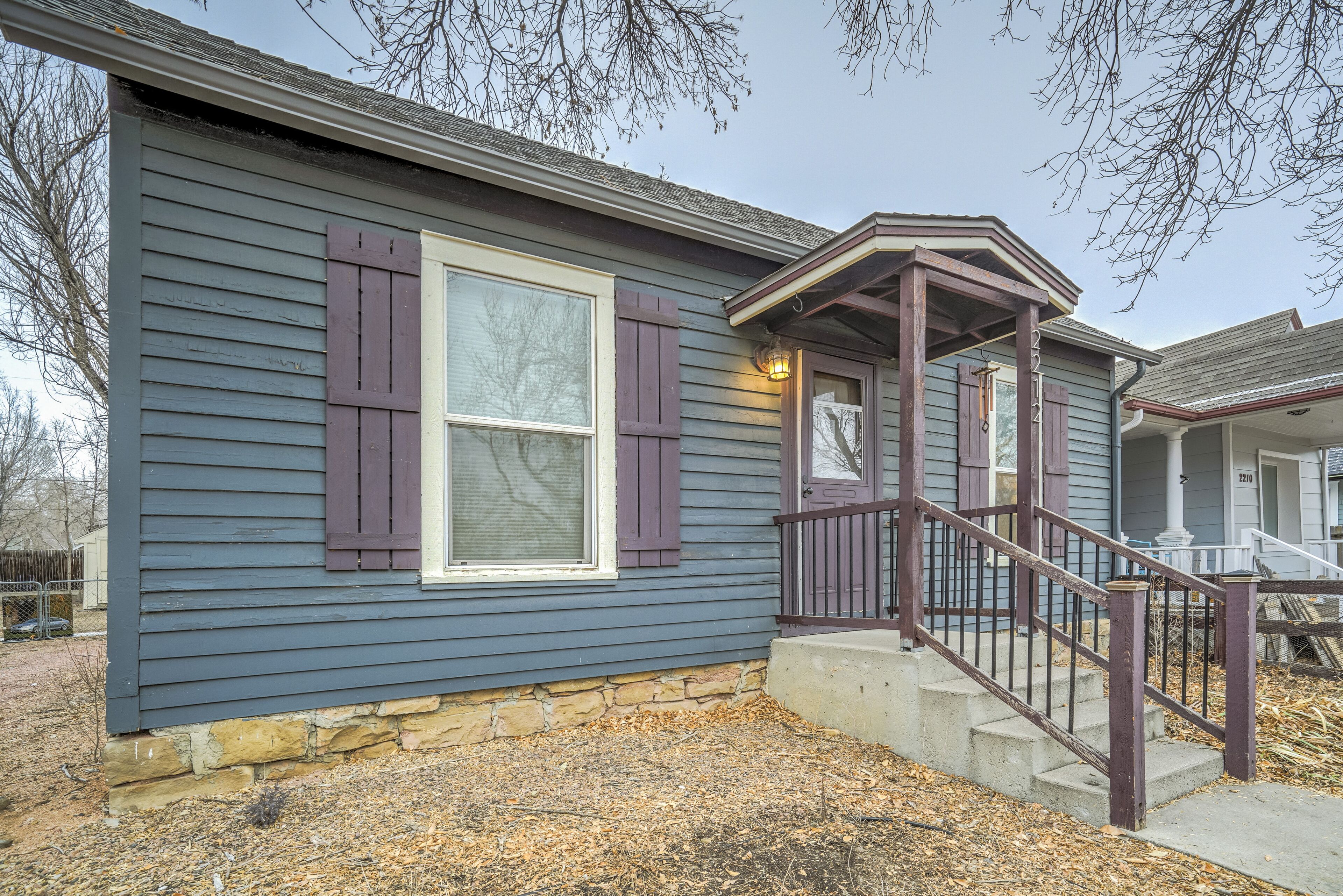 A house with a stone foundation, a front porch with a staircase, and a window with shutters.