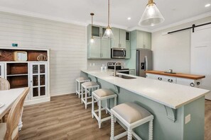 A kitchen with a central island, bar stools, a microwave, a refrigerator, and pendant lighting.