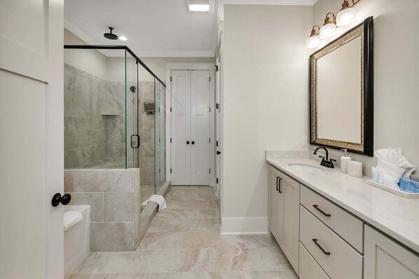 A modern bathroom with a glass-enclosed shower, a large mirror, and a marble-tiled floor.