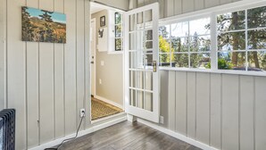 A room with a large window, a door leading to another room, and a painting on the wall. - Pete's Place (Woodland Park)