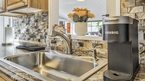 A modern kitchen with a stainless steel sink, a Keurig coffee maker, and a backsplash with a marble pattern. - Pete's Place (Woodland Park)