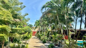 A pathway lined with palm trees and various plants, leading to a building with a red wall. - AJ Paradise Resort (Krabi)