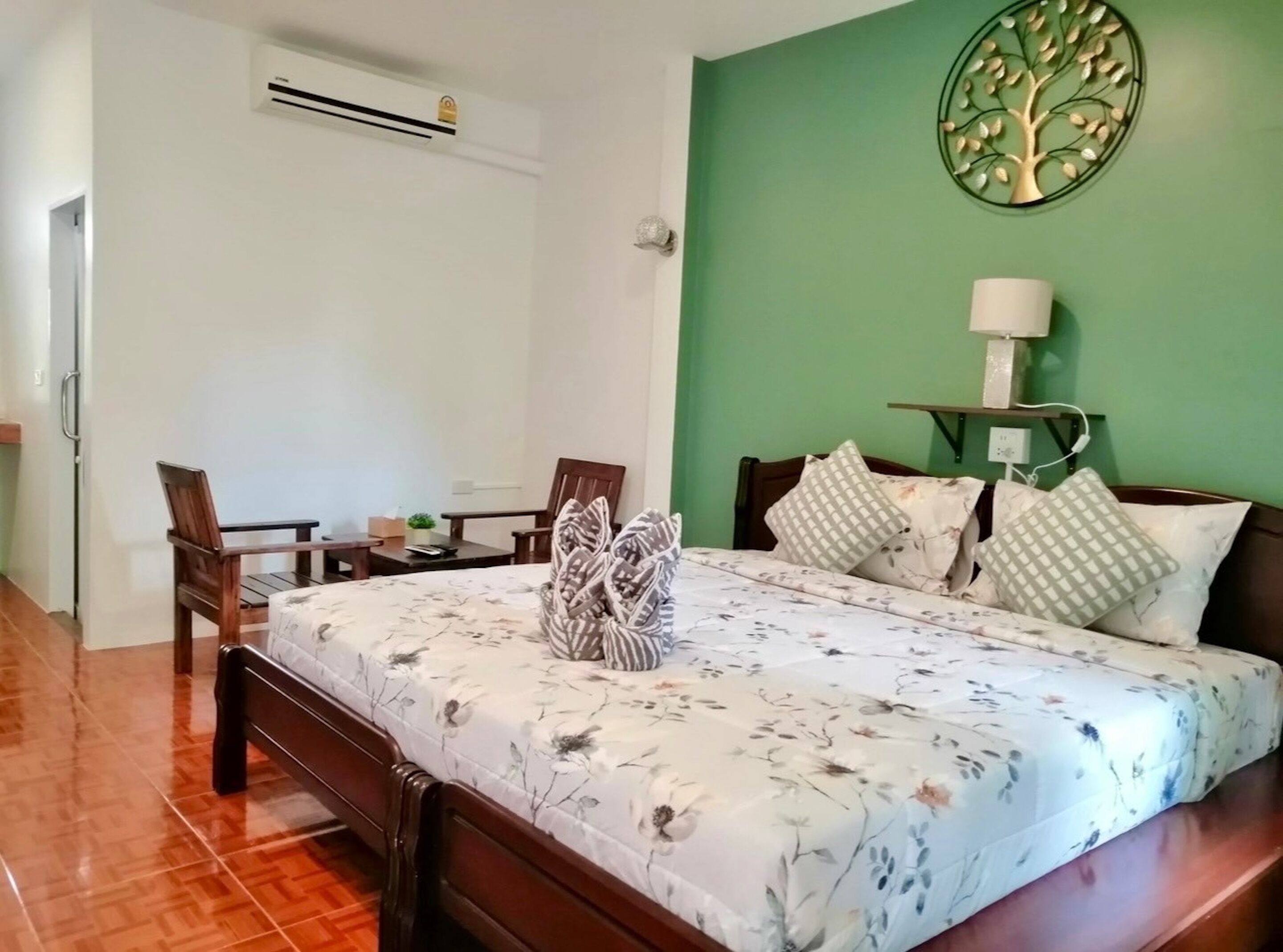Un dormitorio con una cama, dos sillas, una mesita, una lámpara de pared y una obra de arte decorativa con forma de árbol.