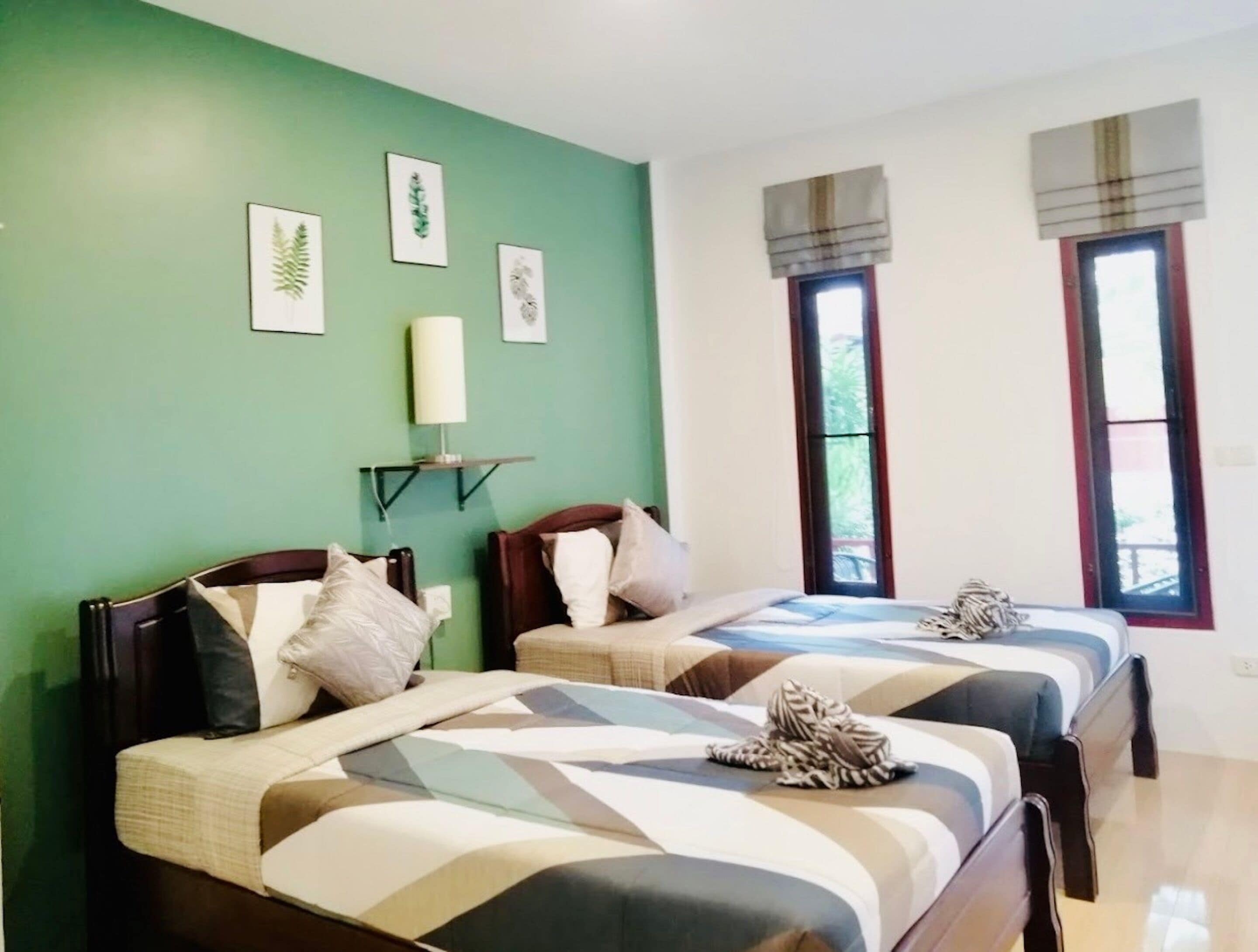 A room with two beds, green walls, and framed pictures.