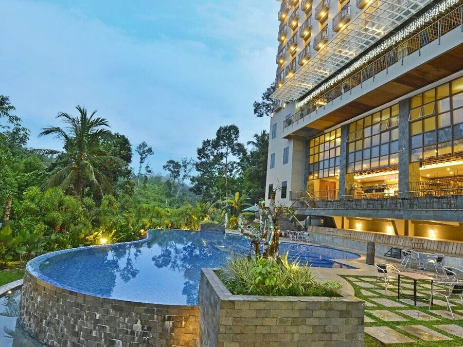 Un hotel con una grande piscina esterna, un giardino curato e un edificio a più piani con balconi.
