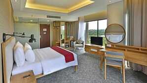 A hotel room with a bed, desk, chair, TV, and a large window offering a view. - FamVida Hotel Lubuklinggau Powered by Archipelago (Lubuklinggau)
