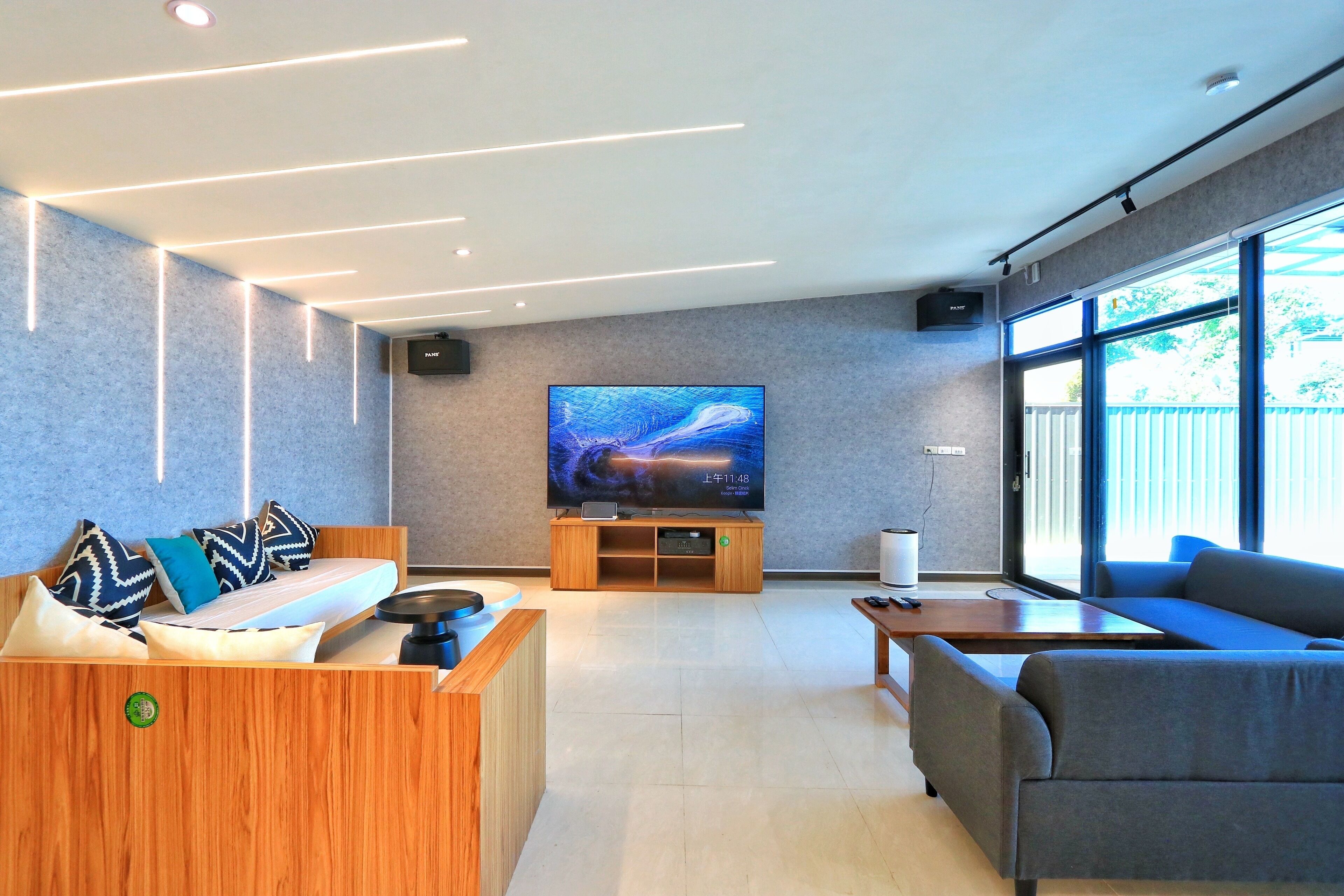 Een moderne woonkamer met een grote flatscreen televisie, houten meubels en grote ramen.