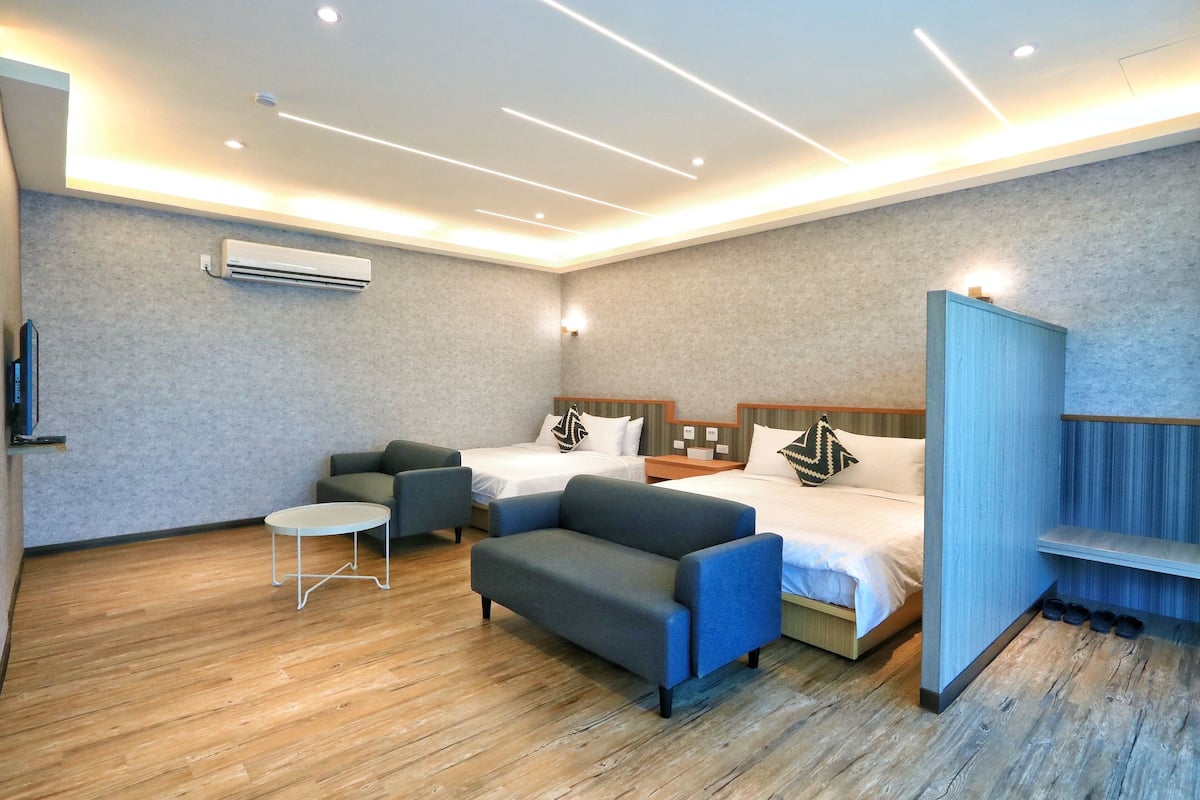 A modern hotel room with two beds, a sofa, a small table, and a TV.