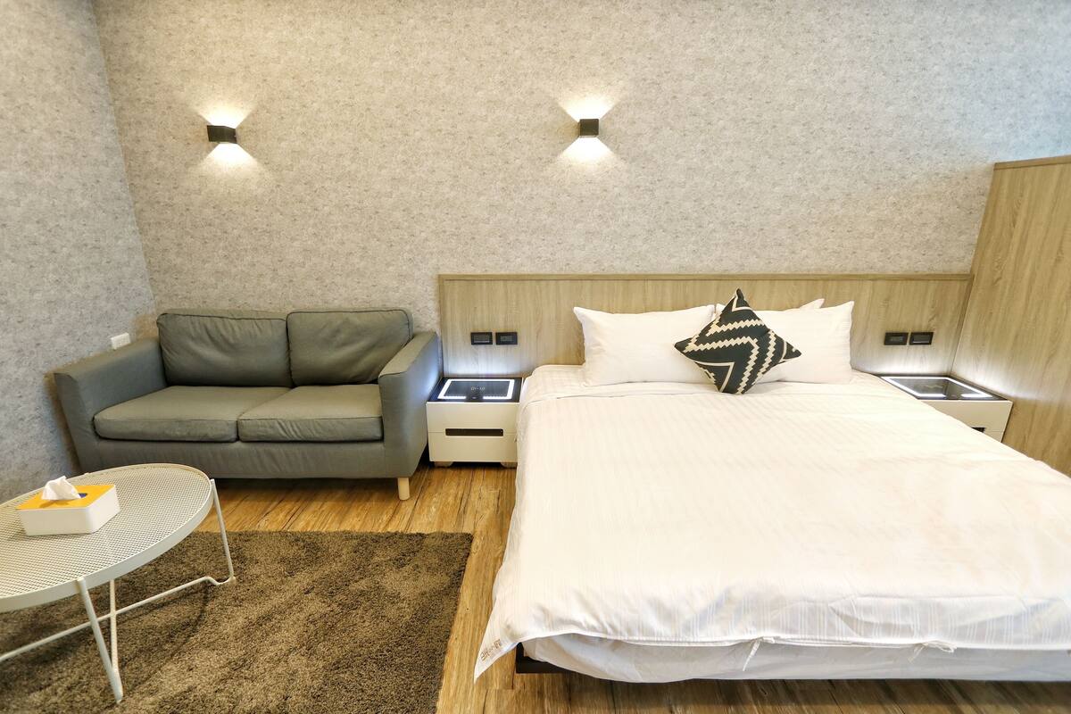 A hotel room with a bed, a grey sofa, a small table with a tissue box, and two bedside tables with lamps.