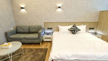 A hotel room with a bed, a grey sofa, a small table with a tissue box, and two bedside tables with lamps.