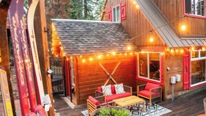 Een houten chalet met schuin dak, een overdekt terras met zitplaatsen en lichtjes.