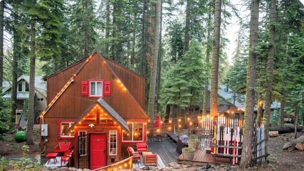 Een chalet met een houten gevel, een rode deur en een terras met buitenmeubels.