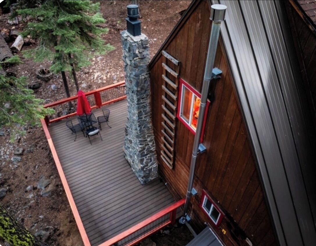 Een houten terras met buitenmeubilair, een stenen schoorsteen en een metalen hekwerk.