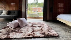 Ein Schlafzimmer mit einer Schlafgalerie, einem großen Fenster, einem Bett, einer Couch und einem flauschigen Teppich.