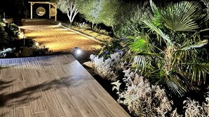 Un espace extérieur aménagé pour la nuit, avec une terrasse en bois, une balançoire et diverses plantes.
