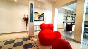 Un intérieur moderne avec un sol à carreaux, un fauteuil rouge en forme de cœur, un vase rempli de fleurs et un tableau accroché au mur.