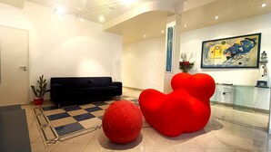 Un hall d’entrée moderne avec un canapé noir, des fauteuils en forme de sac de haricots rouges, un sol à carreaux et un tableau accroché au mur.
