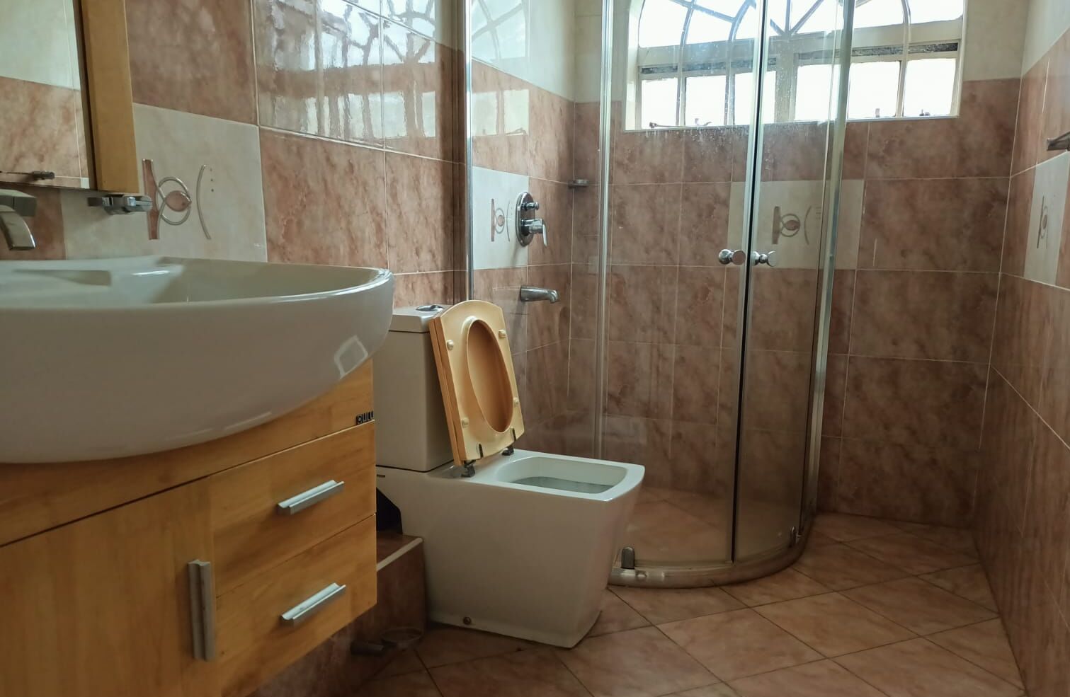 Un baño con lavamanos, un mueble de madera, inodoro y una cabina de ducha con mampara de vidrio.