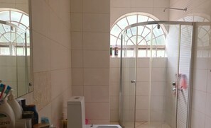Enjoy a refreshing shower in the bathroom, featuring a glass-enclosed shower area, a large mirror, a toilet, and a sink with a soap dispenser.
