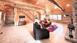 Ein Blockhaus-Interieur mit Treppe, Kamin und Wohnbereich mit Sofa und Couchtisch.