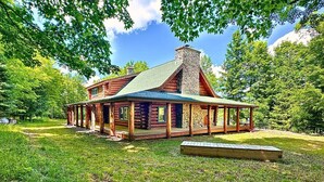 Eine Blockhütte mit Steinkamin, Holzveranda und einem grünen Rasen.