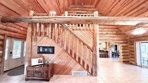 Ein Holzblockhaus-Interieur mit einer Holztreppe, einem Essbereich und einem Kamin.