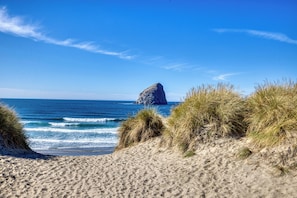 A beach with sand dunes, a rock formation in the distance, and the ocean.