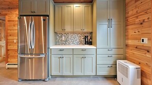 A compact kitchen with light-colored cabinets, a stainless steel refrigerator, a tiled backsplash, and a built-in air conditioning unit.