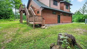 A two-story wooden house with a deck, a staircase, and a green door.