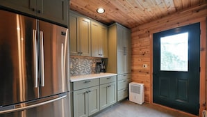 A kitchen with a stainless steel refrigerator, light green cabinets, a tiled backsplash, and a black door with a window.