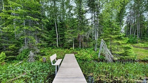A wooden dock extending into a forested area with a bench on one end.