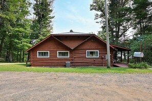 Une cabane en rondins avec un porche, une boîte aux lettres et une allée gravillonnée.