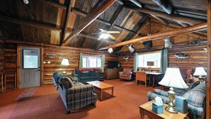 L’intérieur d’une cabane en rondins, avec un plafond haut, des murs en bois, des meubles à motifs écossais et des têtes d’animaux fixées au mur.