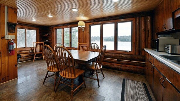 L’intérieur d’un chalet en bois comprend une table et des chaises, de grandes fenêtres et un coin cuisine.