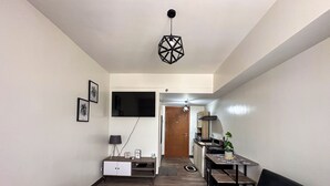 A compact hotel room with a bed, a desk with a chair, a sofa, a TV mounted on the wall, and a small kitchenette. - A cozy home in the middle of the city (Cebu City)