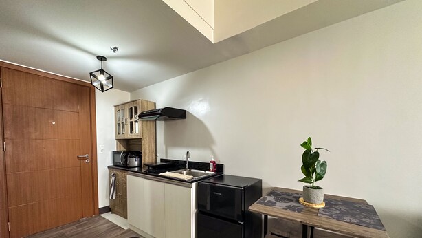 A compact kitchen with a black refrigerator, a wooden cabinet, and a small dining table with a potted plant. - A cozy home in the middle of the city (Cebu City)
