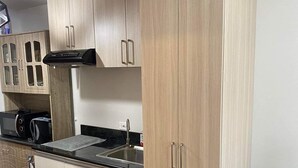 A modern kitchen with light wood cabinets, a black refrigerator, and a stainless steel sink. - A cozy home in the middle of the city (Cebu City)