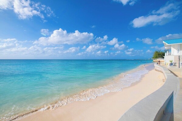 A beach with clear turquoise water, a sandy shore, and a building with a blue roof.