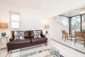 A modern living room with a brown leather sofa, two side tables with lamps, a glass coffee table, and wooden chairs.
