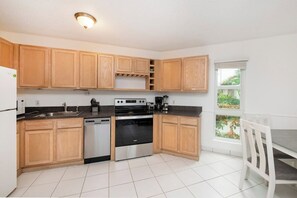 A kitchen with wooden cabinets, a dishwasher, a stove, and a window with a view of greenery.