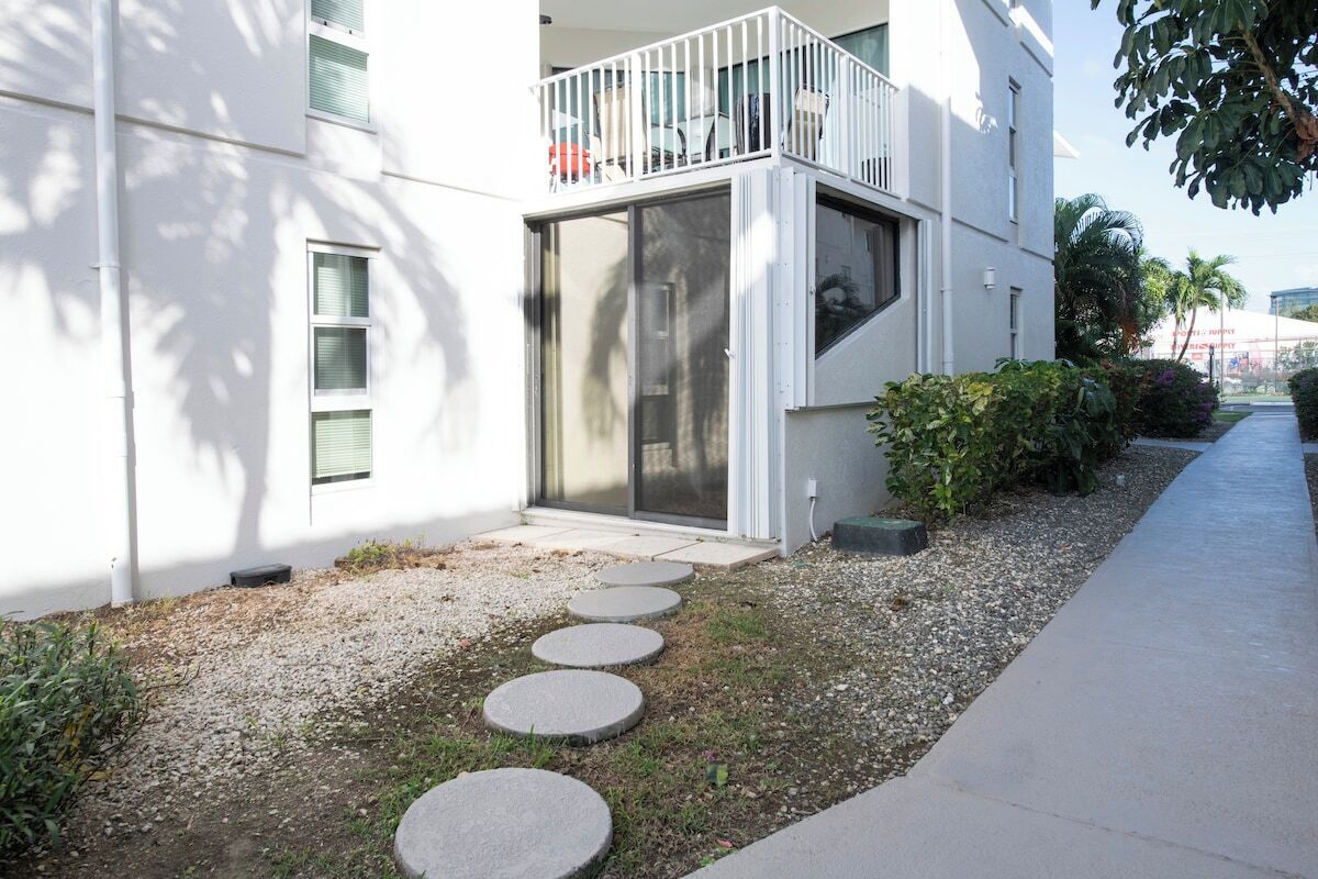 A modern building with a balcony, a gravel pathway with stepping stones, and a sidewalk.
