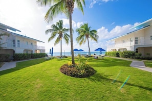 A resort with multiple-story buildings, a well-maintained lawn, palm trees, and a view of the ocean.