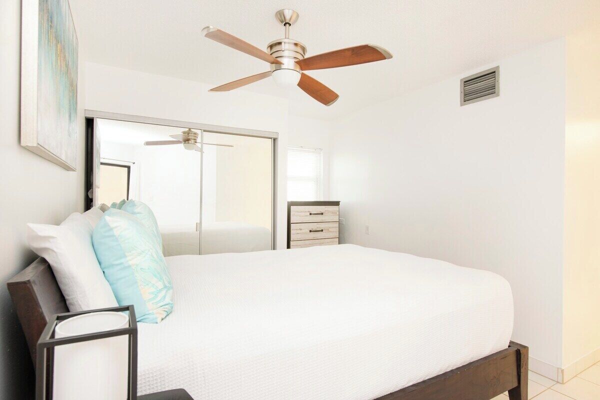A bedroom with a bed, a ceiling fan, a dresser, and a mirror.