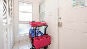 Un passadís amb una porta blanca, una finestra amb persianes i un carretó vermell per equipatge.