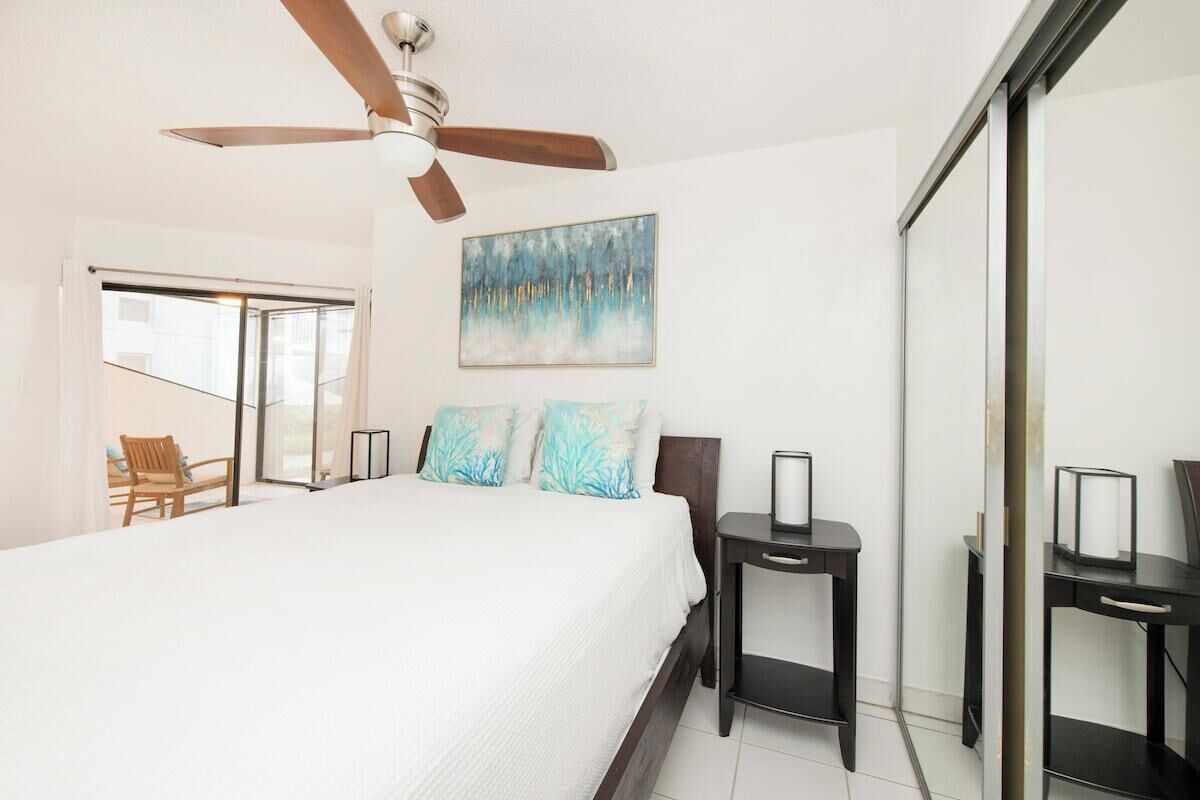A bedroom with a bed, a ceiling fan, a painting, and a chair.