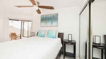 A bedroom with a bed, a ceiling fan, a painting, and a chair.